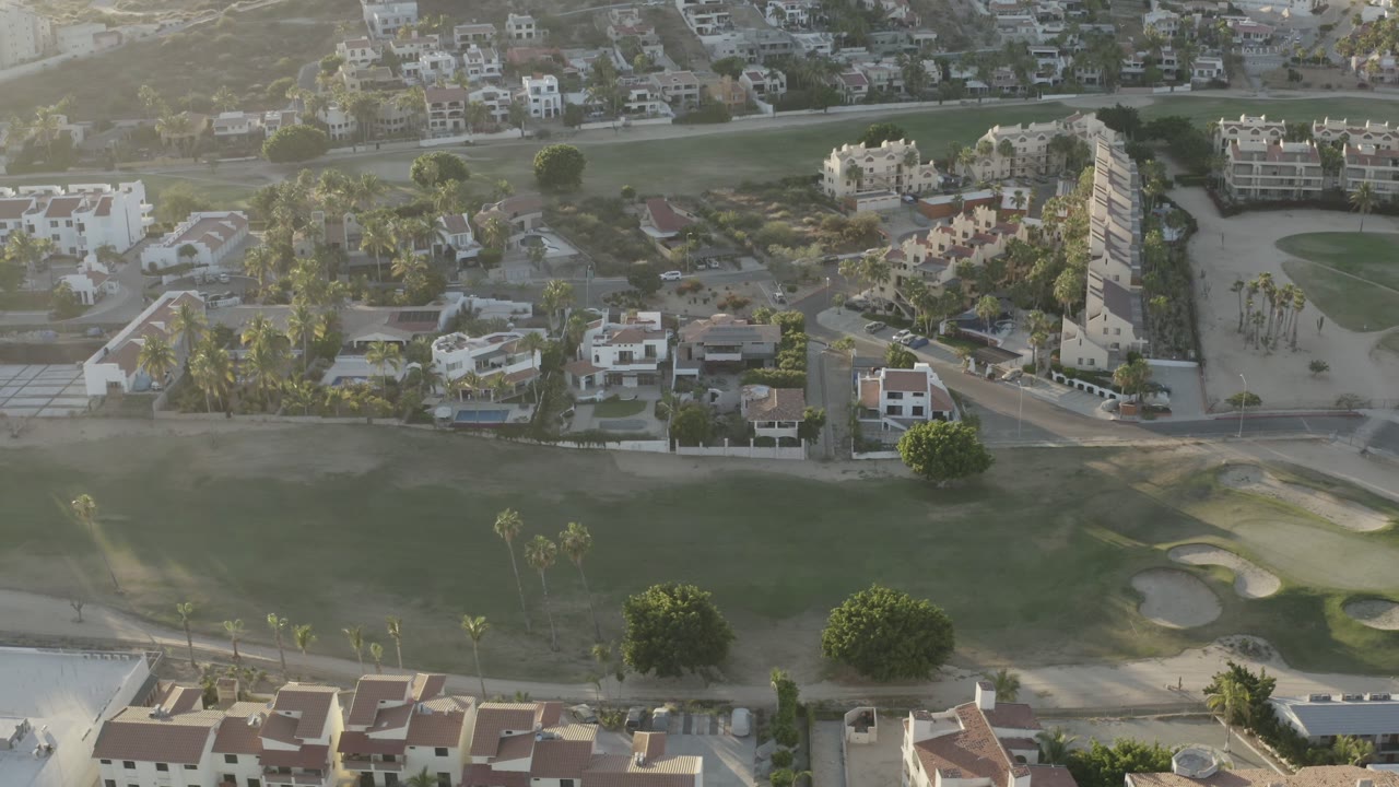 Aerial residential view with a road, villas, palms, and open turf.