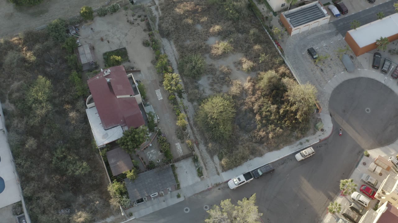 Overhead view of homes, a cul-de-sac, parked cars, and dry vegetation.