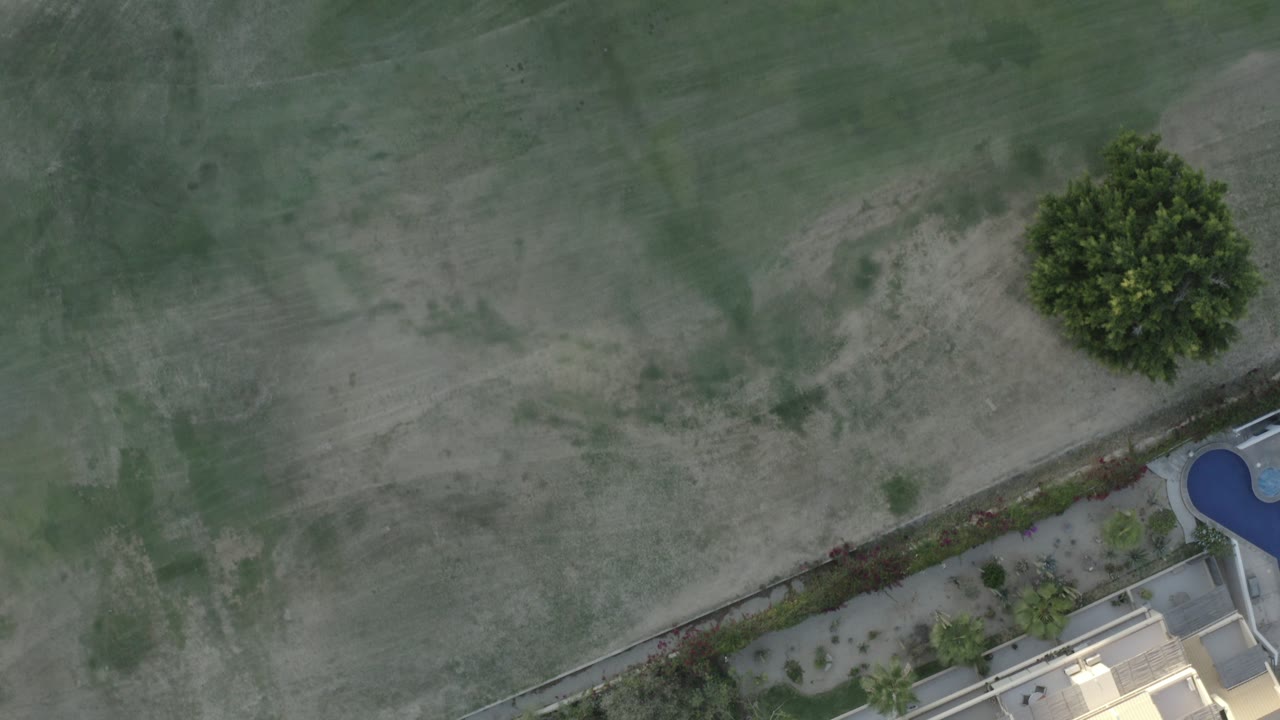 Top-down view of shallow green water, pale sand, and the edge of a beachfront property.