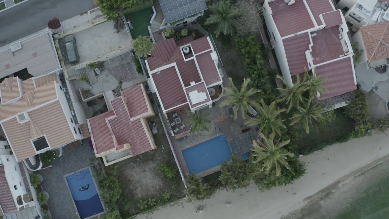 Aerial view of houses and pools with palms along a sandy beachfront.