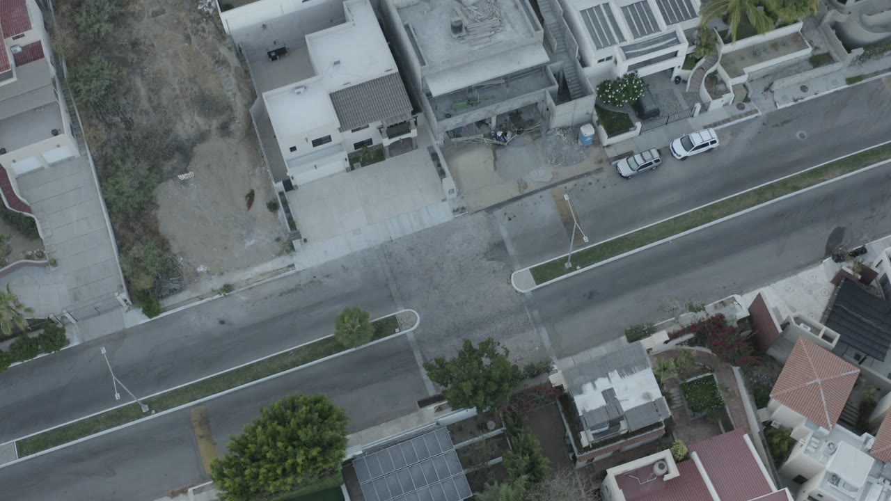 Overhead view of houses, a street, parked cars, and dry lots.