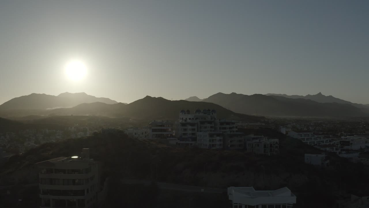 Low sun above mountains with a white building in the foreground.