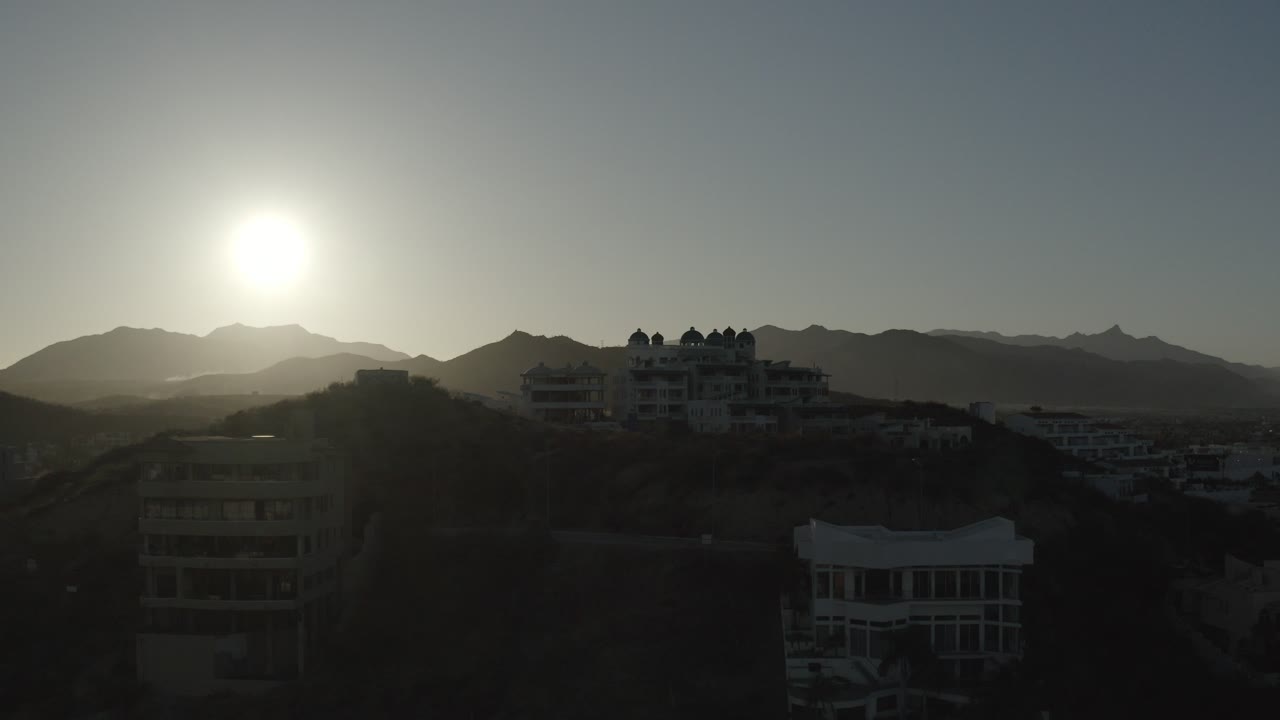 Sun over dark hillside condos and distant mountains at sunset.