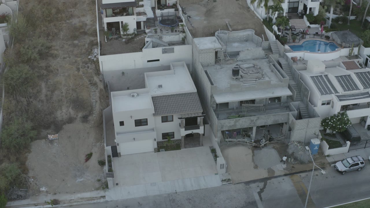 High aerial view of modern houses, dry lot, street, parked car, and pool.