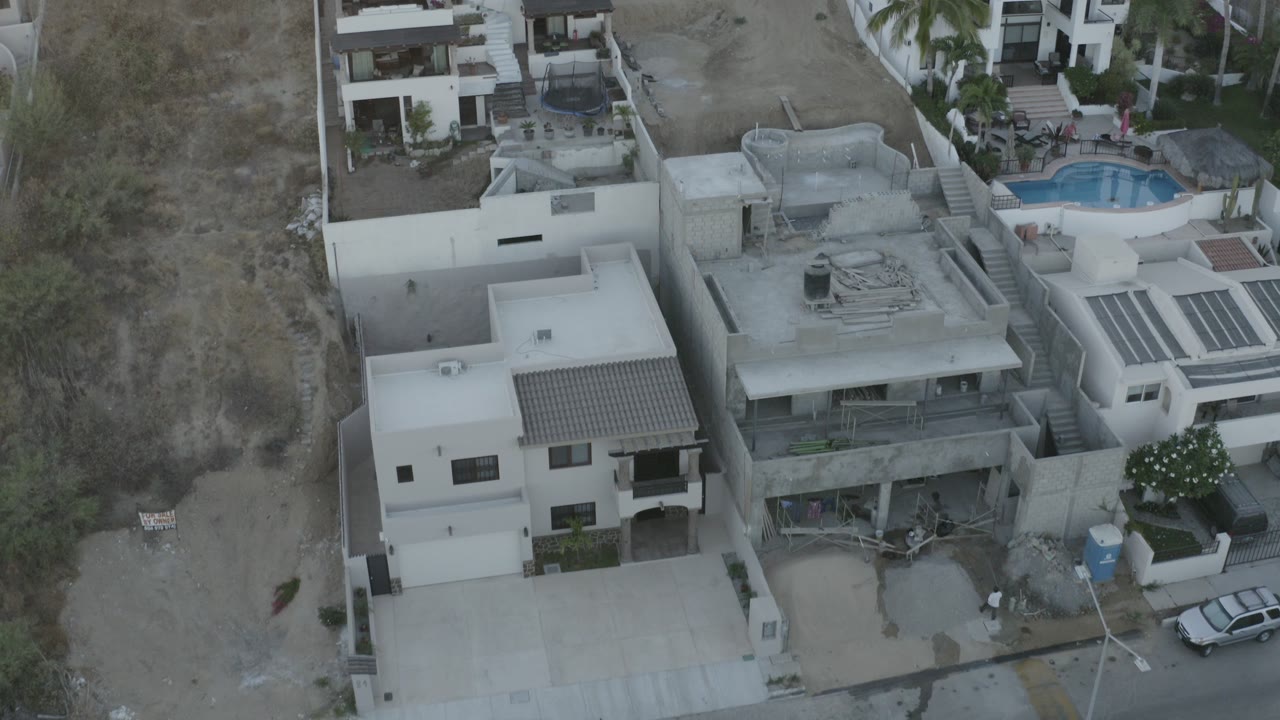 Aerial view of modern white homes beside a small private pool and dry hillside lots.