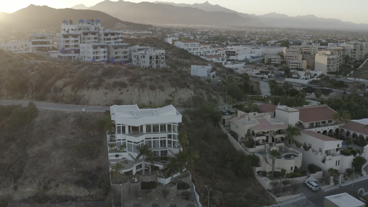 Elevated view of hillside homes and distant mountains at low sun.