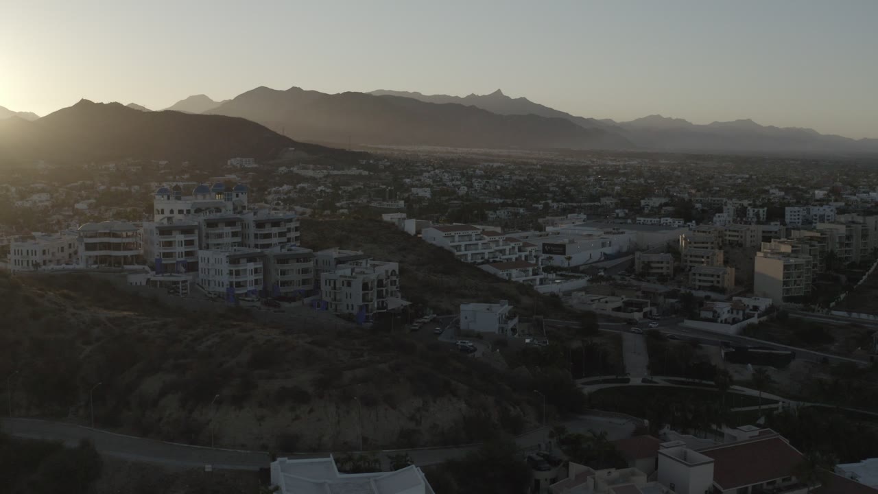 Aerial view of hillside buildings and mountains with sun at the left edge.