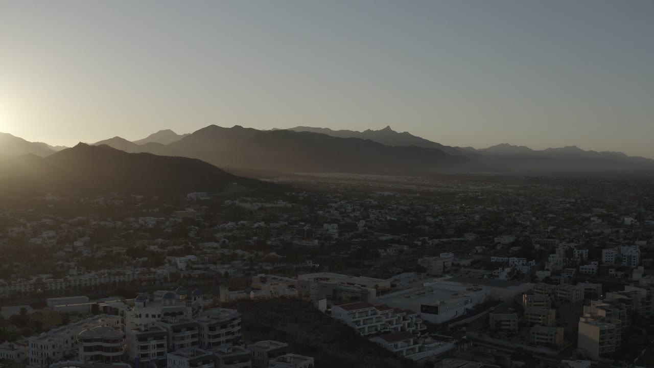 Sun rising beside dark mountain ridges above a shadowed town.