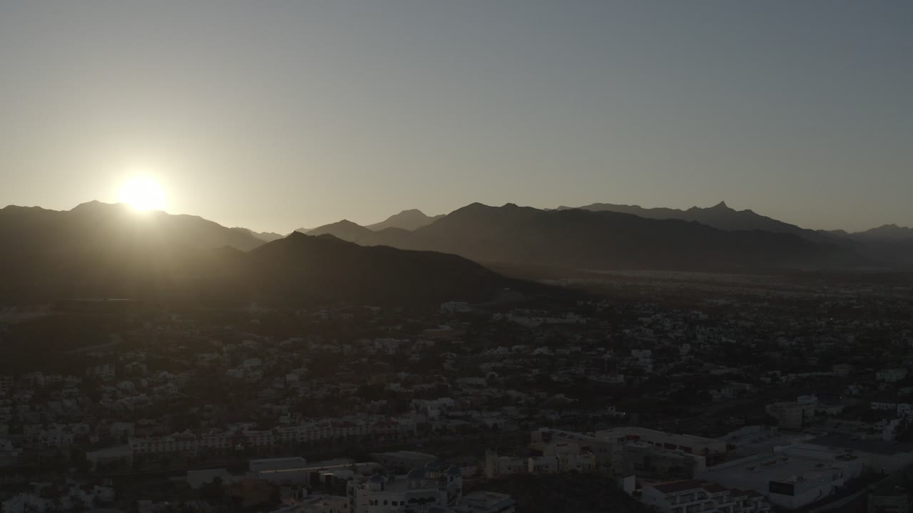 Low sun above dark mountains and a shadowed city foreground.