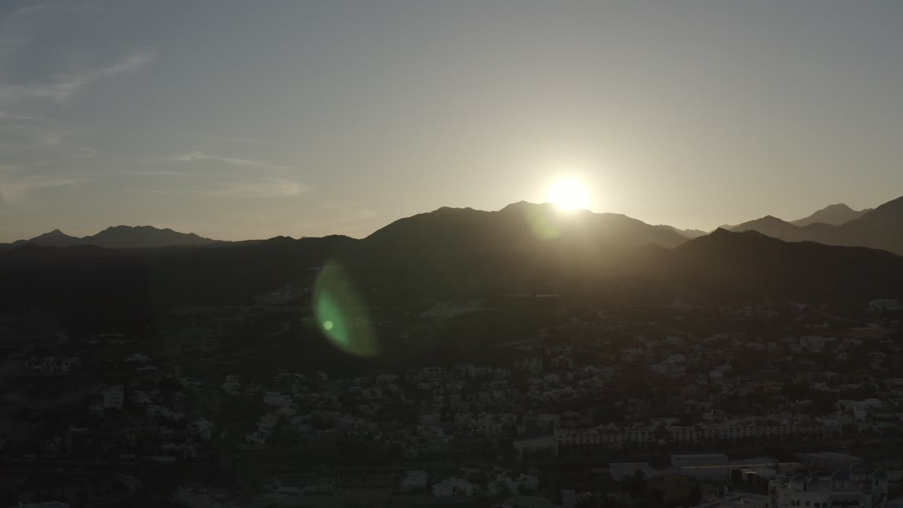 Sun rising over dark mountain ridges above a shadowed town.