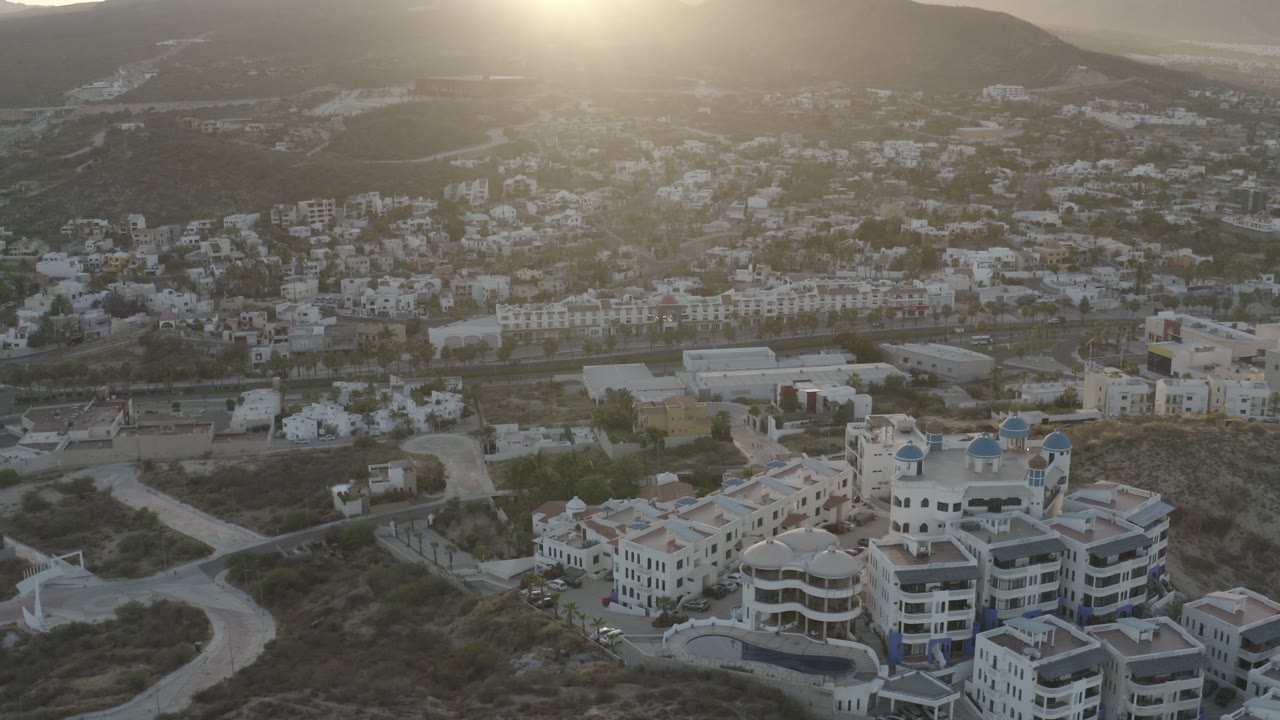 Aerial view of sunlit buildings below mountains.