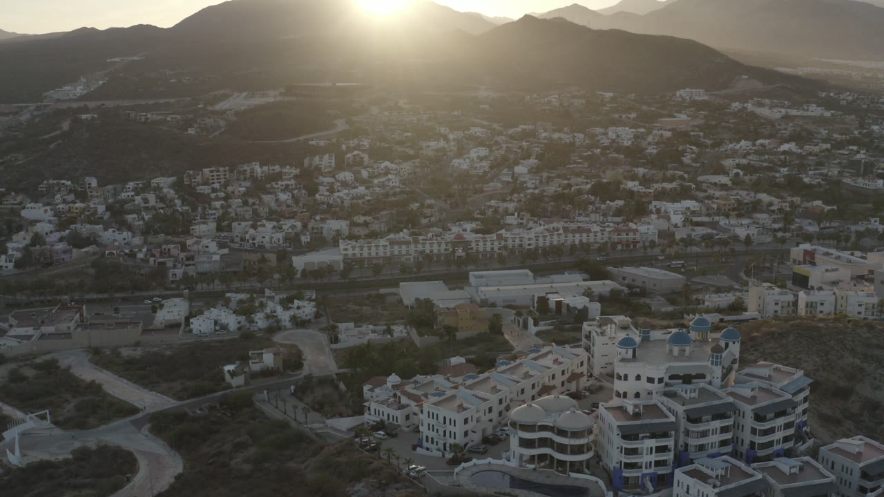 Aerial sunrise over white hillside buildings and mountains.
