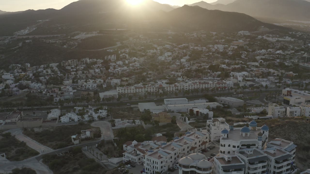 Sunlit valley with white buildings below dark mountains.