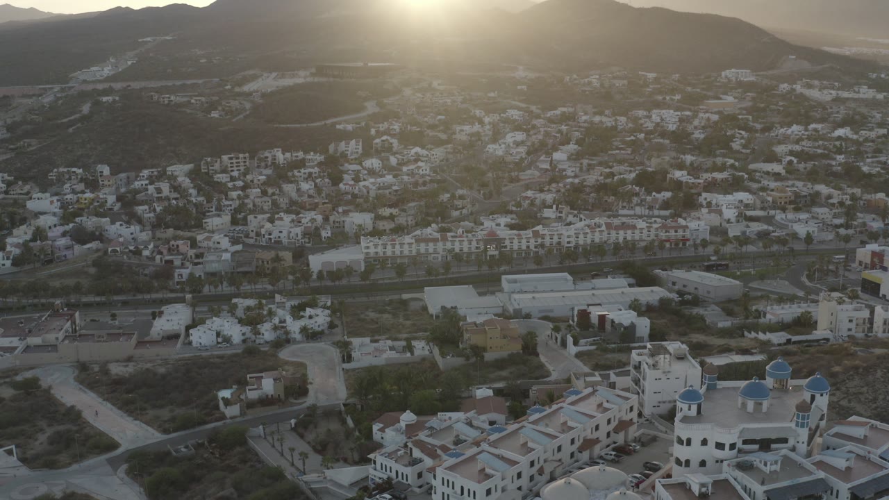 Aerial view of hillside buildings below a bright low sun.