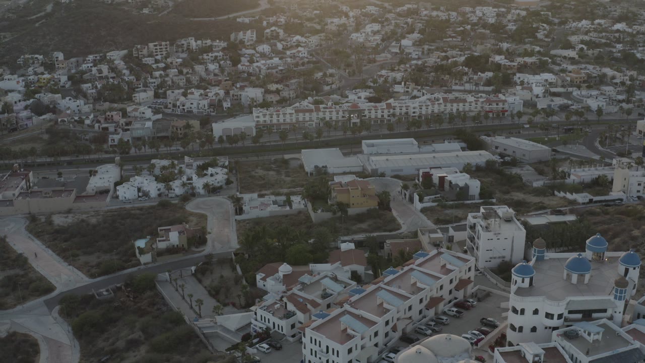 Aerial view of white buildings, roads, and hillside homes.
