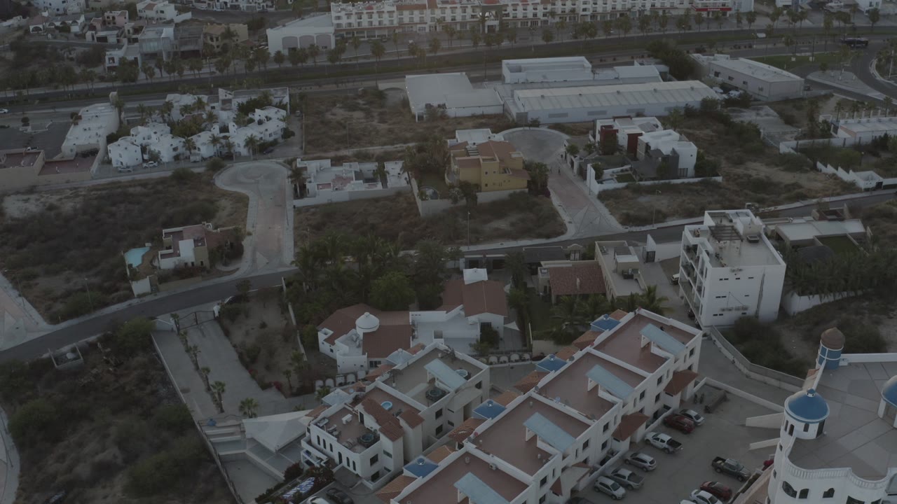 Drone view of a quiet housing area with white walls, roads, and parked cars.