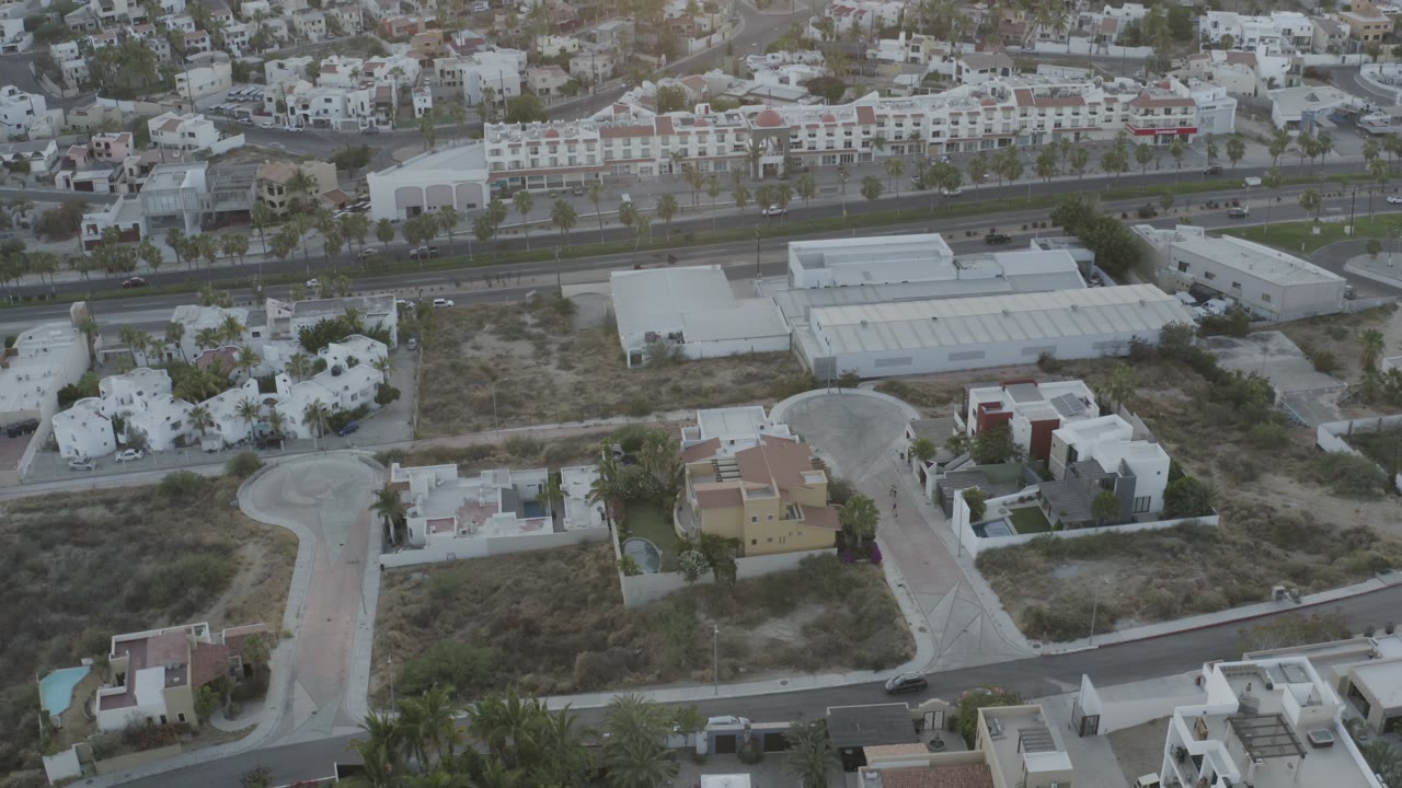 Drone-height view of a sandy block, villas, palms, and road traffic
