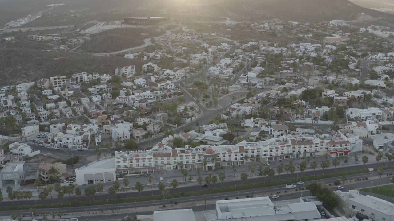 Aerial neighborhood view with road, cars, palms, and mountains.