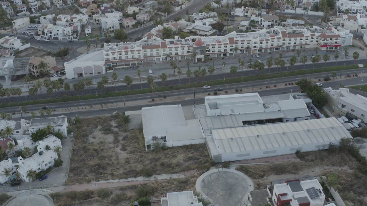 High aerial view of white buildings, homes, a divided road, and dry lots.