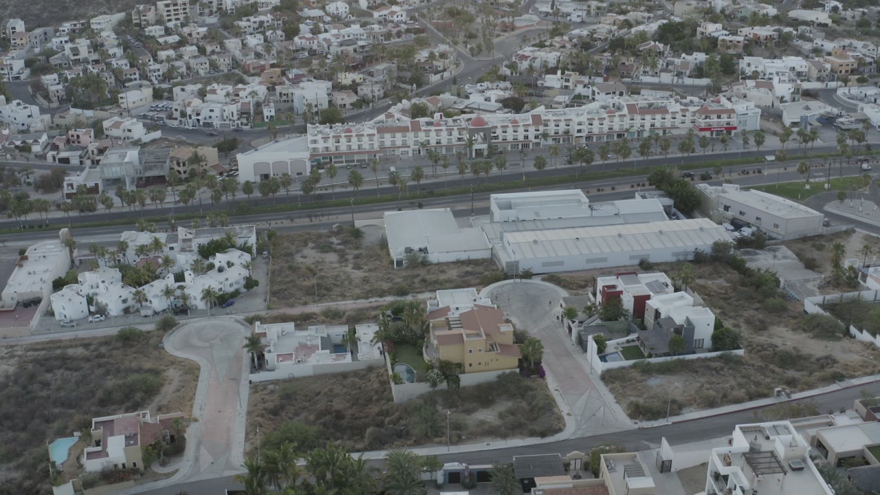 Aerial view over hillside homes, roads, dry lots, and palm trees.