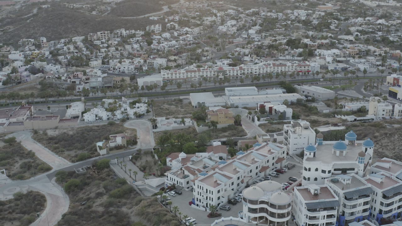 Aerial view of white resort buildings below a hillside town.