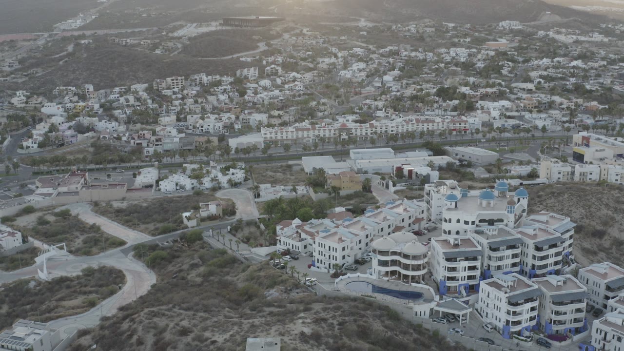 Aerial view over hillside homes, roads, distant water, and mountains.