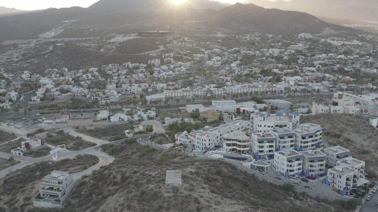 Aerial sunrise view over hillside buildings and mountains.