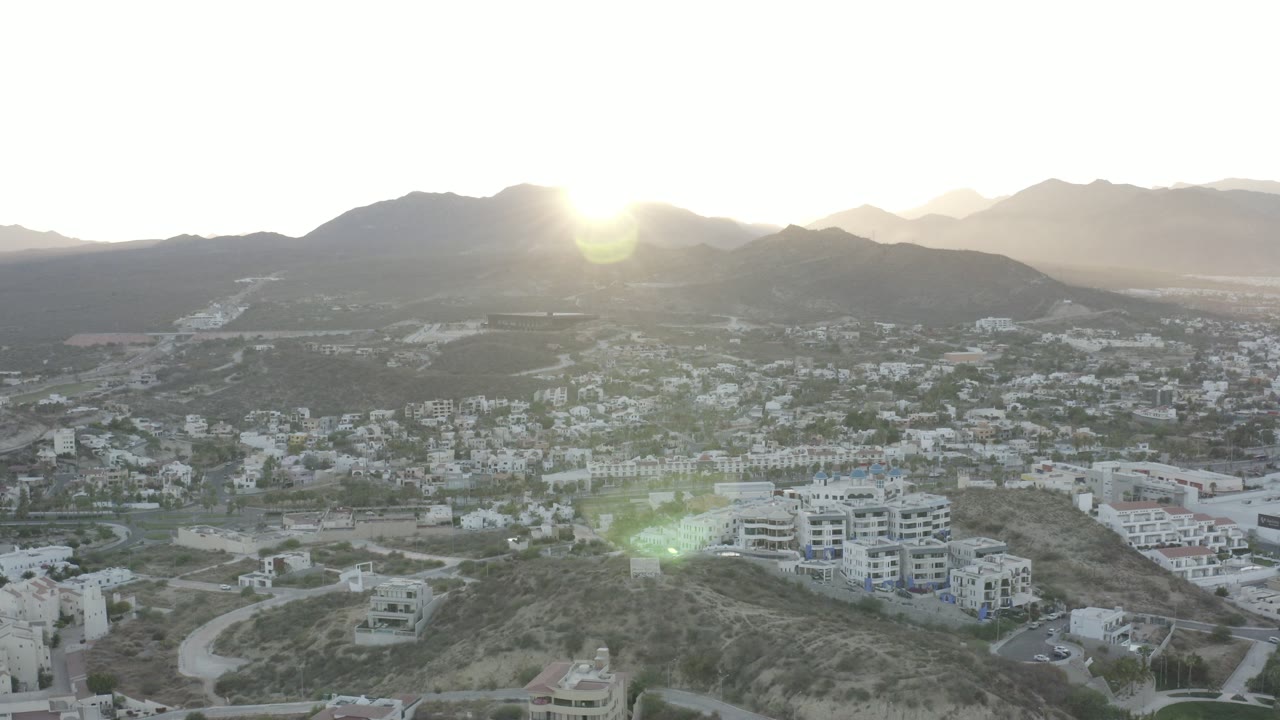 Aerial view of hillside town below mountains with low sun glare.