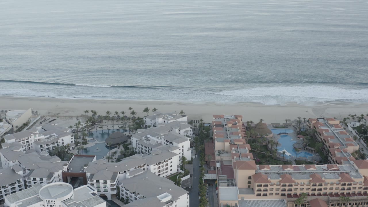 Aerial view of ocean waves, beach, and beachfront apartment buildings.