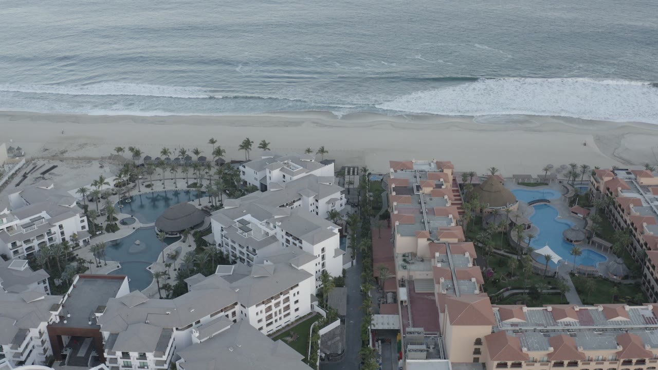 Resort complex beside a wide beach with ocean waves beyond.