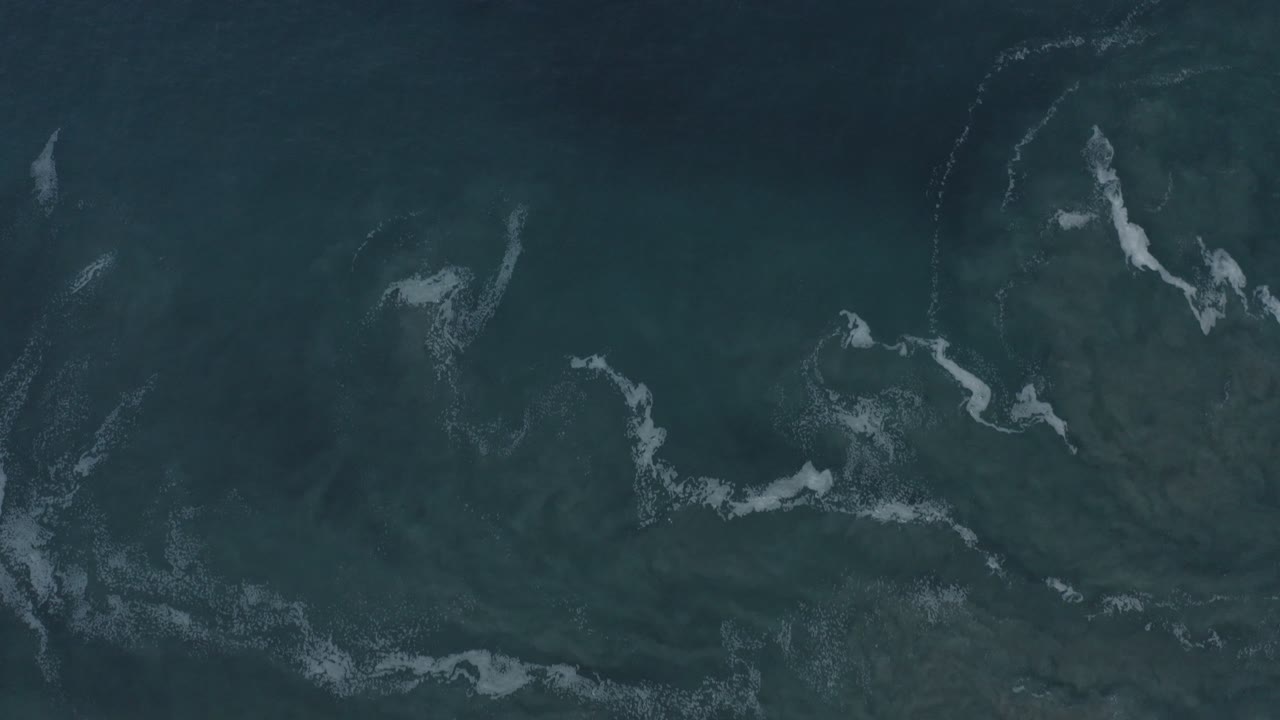 Dark ocean water with broken white foam lines from an overhead angle.
