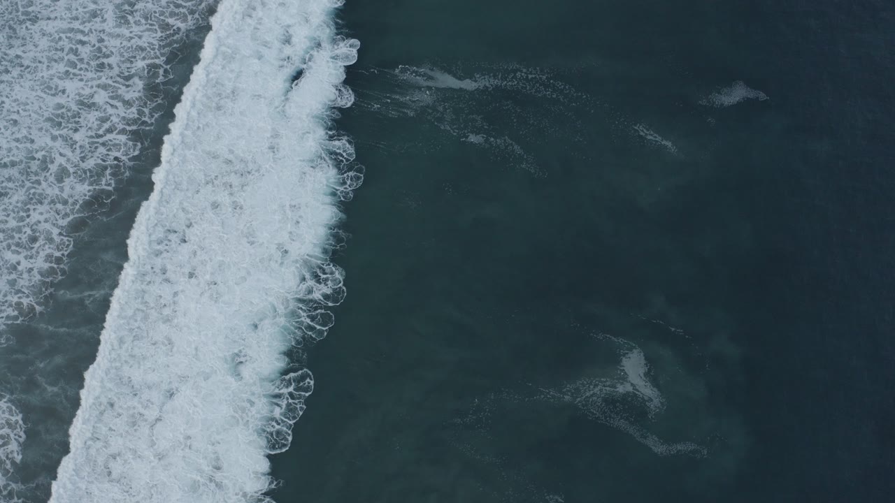 Foamy wave band beside open blue-green water.