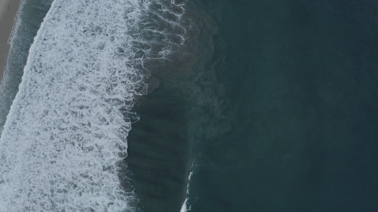 Top-down surf breaking beside a narrow sand edge.