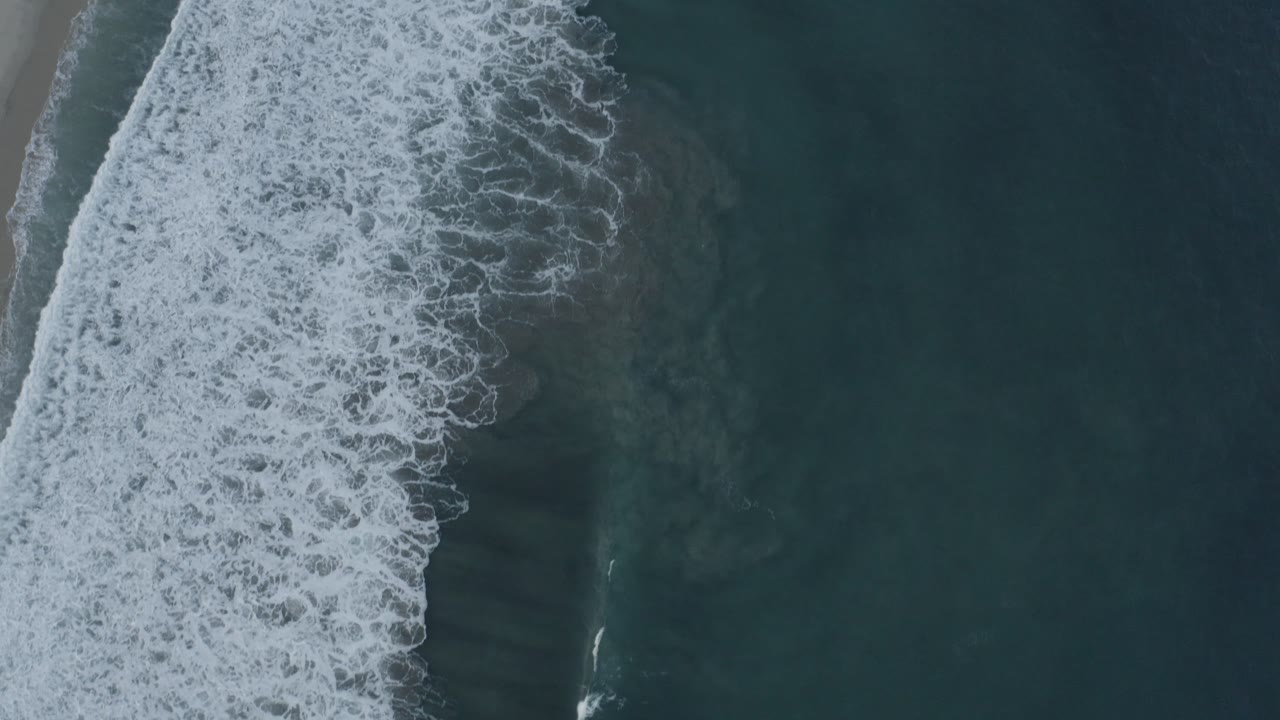 Dense foamy surf line in a vertical overhead beach view.