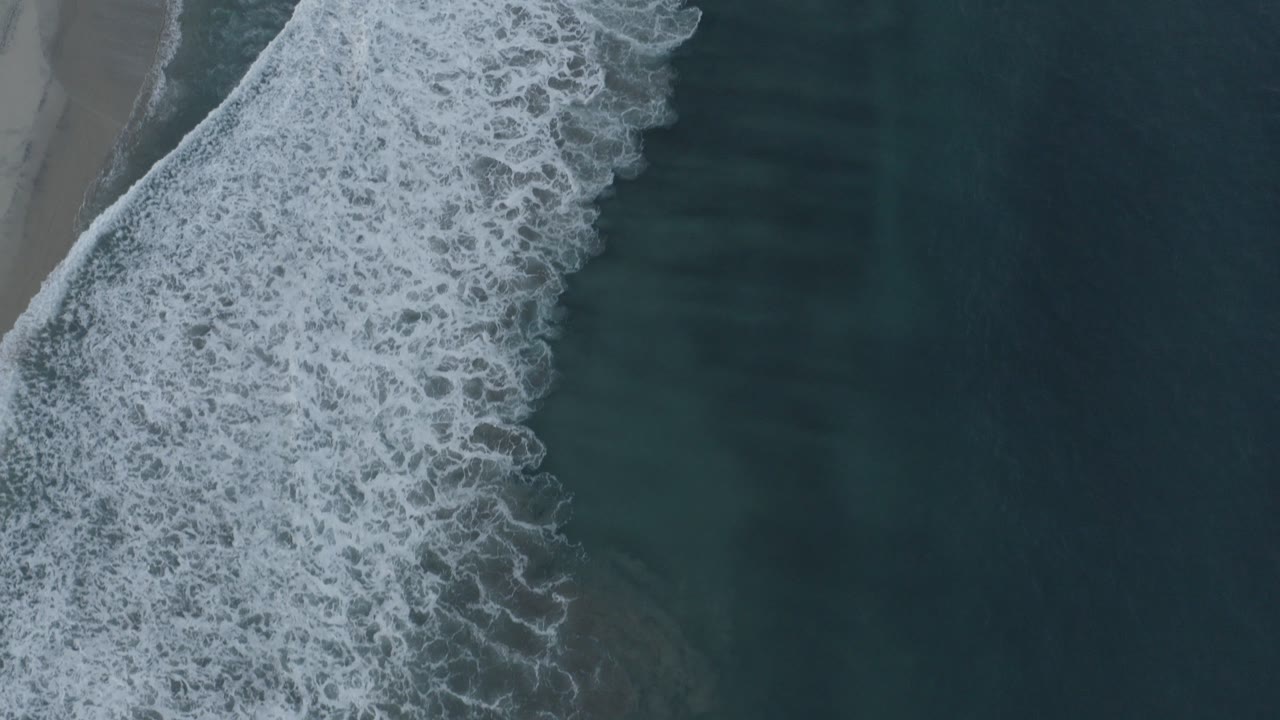 Overhead surf breaking beside a narrow sandy beach.
