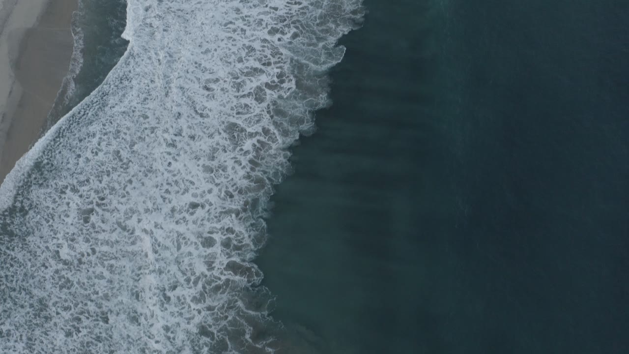 White surf curling along a dark blue-green shoreline.