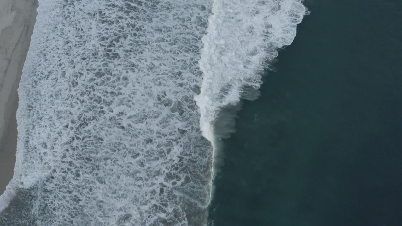 Overhead Los Cabos surf fills the left side while darker water opens on the right, with no visible people in frame.
