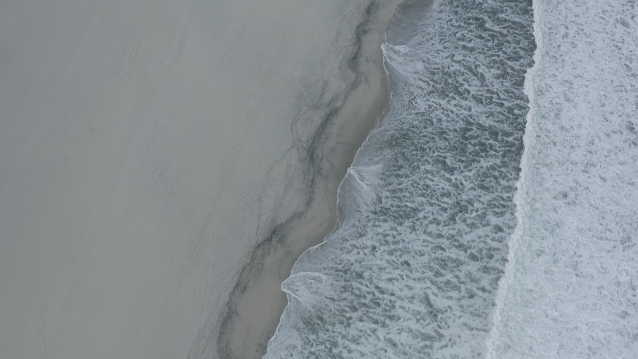 Overhead view of surf foam beside pale sand.