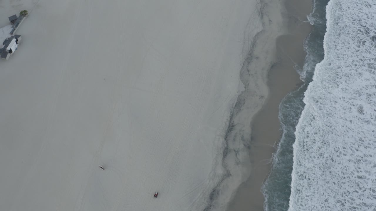 Overhead beach with pale sand and surf along the right edge.