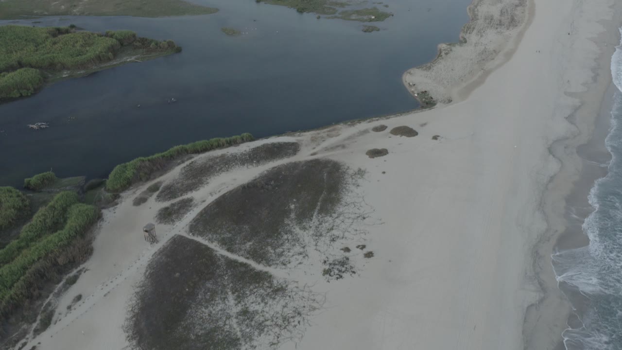 Aerial beach scene with lagoon water, green shrub islands, sand, and surf.