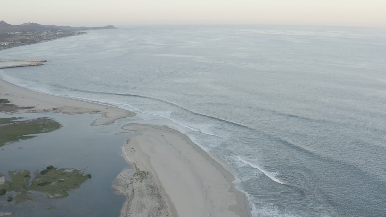 Aerial view of a sandbar, inlet, and pale ocean at dusk.