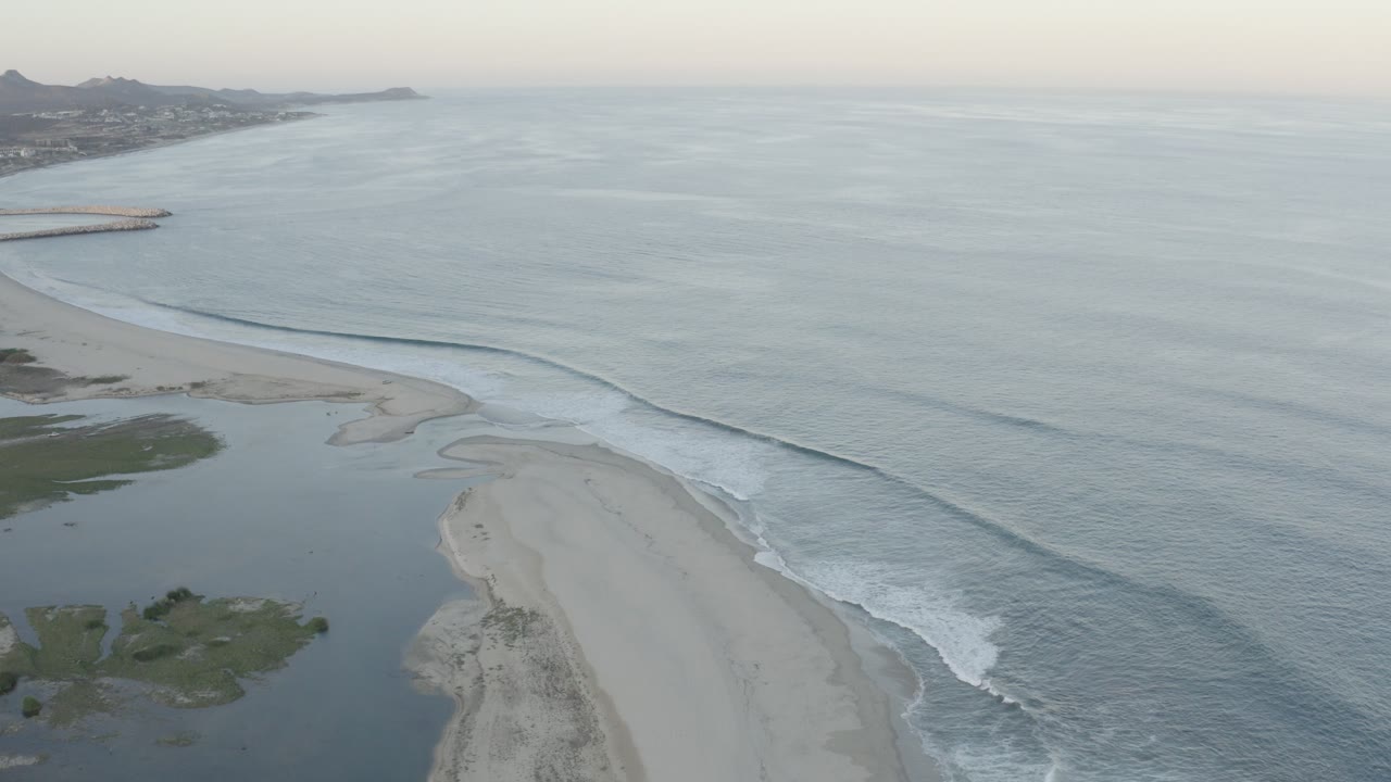 Aerial view of a curved beach, calm surf, and lagoon water.