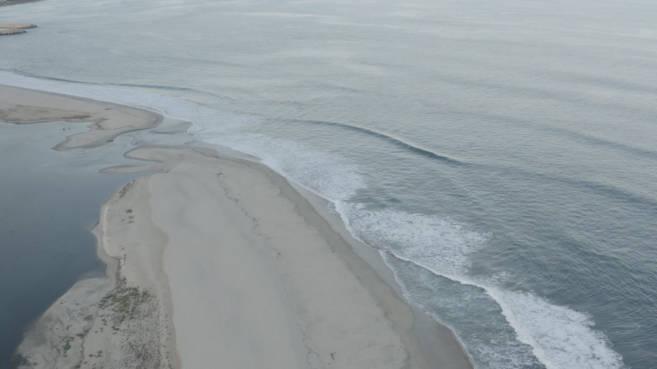 Aerial view of a sand spit between inlet water and ocean waves.