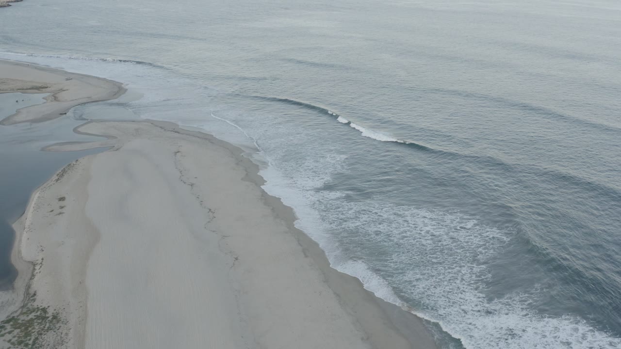 At 0:01, the Los Cabos aerial frame holds on the sandbar as a white wave line breaks along the right side of the shore, with no visible people.