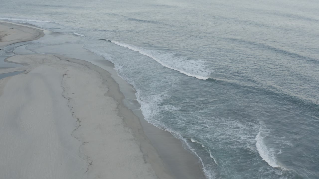 Elevated view of gray surf washing along a pale sandy beach.