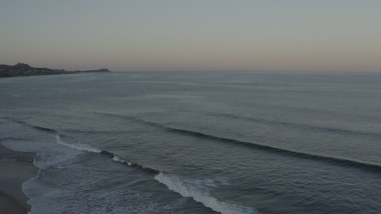 Ocean surf breaks diagonally toward shore beneath a pale sky.