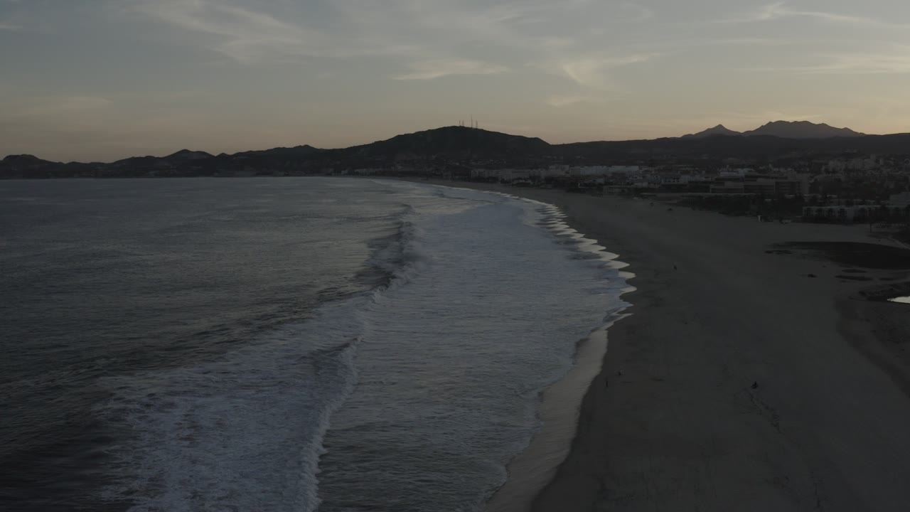 Dim aerial shoreline with ocean, beach, and mountains