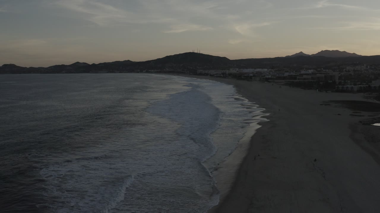Elevated beach view with foamy surf and low hills under fading light.