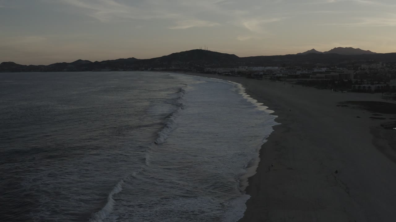 Drone-like view of a beach where waves form white bands near the shoreline.
