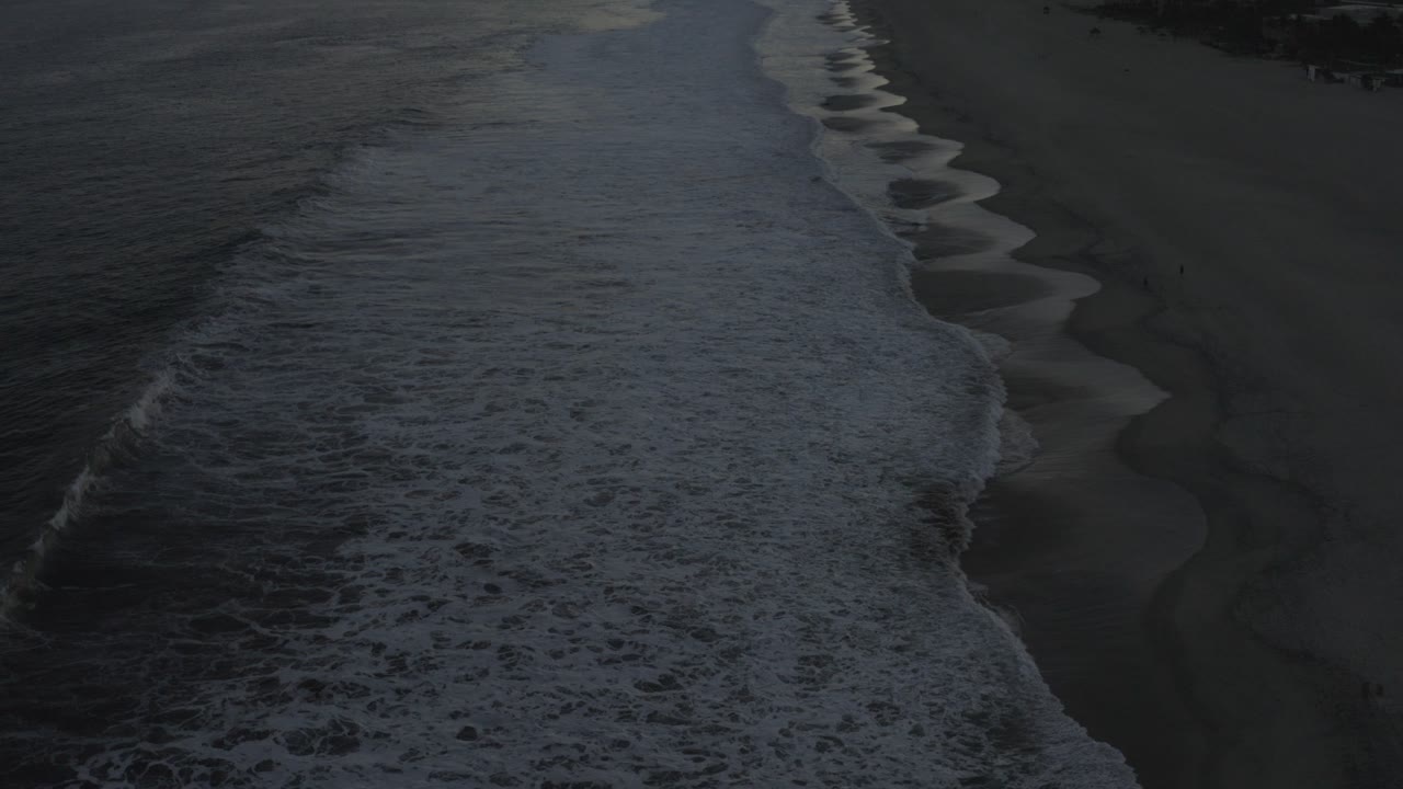 Overhead view of white surf meeting dark wet sand in Los Cabos, Mexico, with no visible people at the start of the clip.